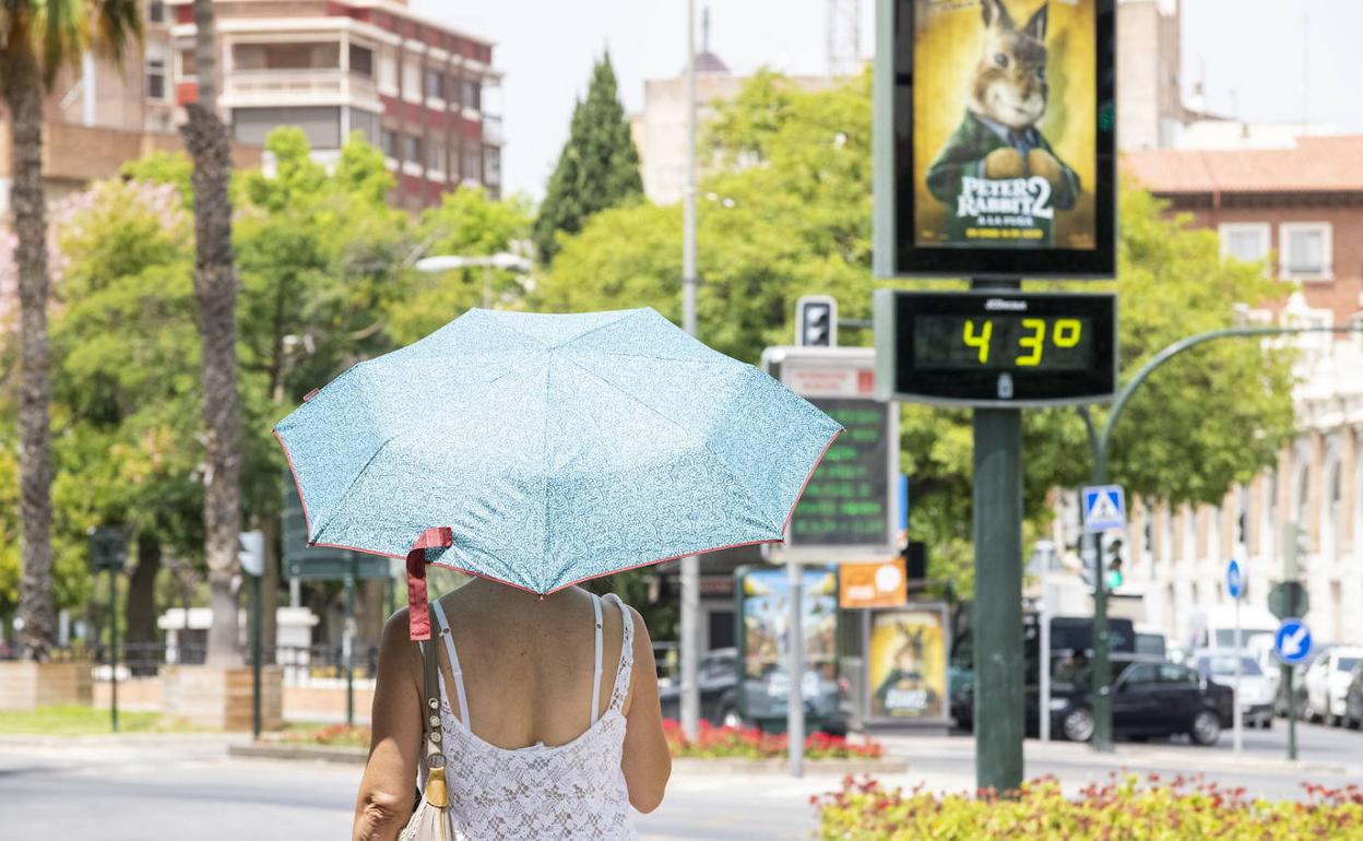 Una mujer pasea por Murcia y, al fondo, un termómetro marca 43 grados, en una imagen de archivo.