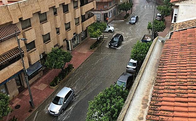 Varios vehículos circulan por una calle de Alhama prácticamente inundada por la lluvia.