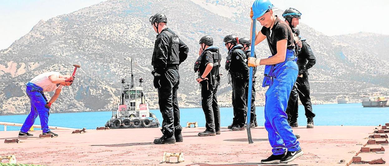 Dos de los tripulantes del mercante trabajan para abrir la bodega en presencia de policías aduaneros, en 2019, en el puerto de Escombreras. 