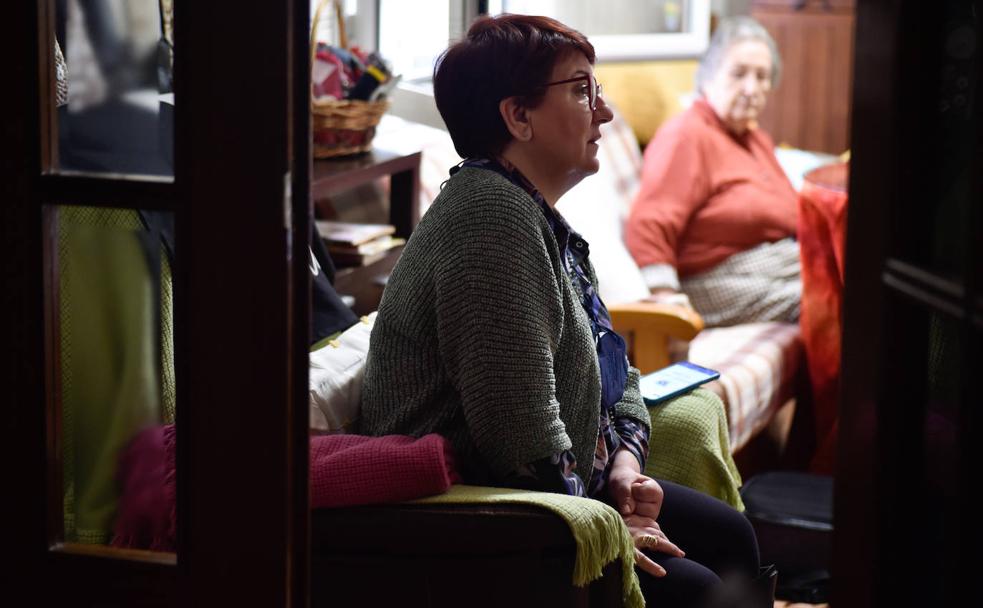 Carmen Guillén, en el sillón del salón de su casa. Al fondo, su madre María, de 88 años, quien la cuida a pesar de sufrir alzhéimer.