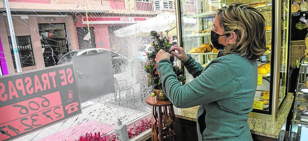 Carmen Solano, dependienta de la panadería La Abuela, ubicada en la calle Carlos III, arregla un adorno, frente al cristal resquebrajado y el cartel de 'Se traspasa'. 