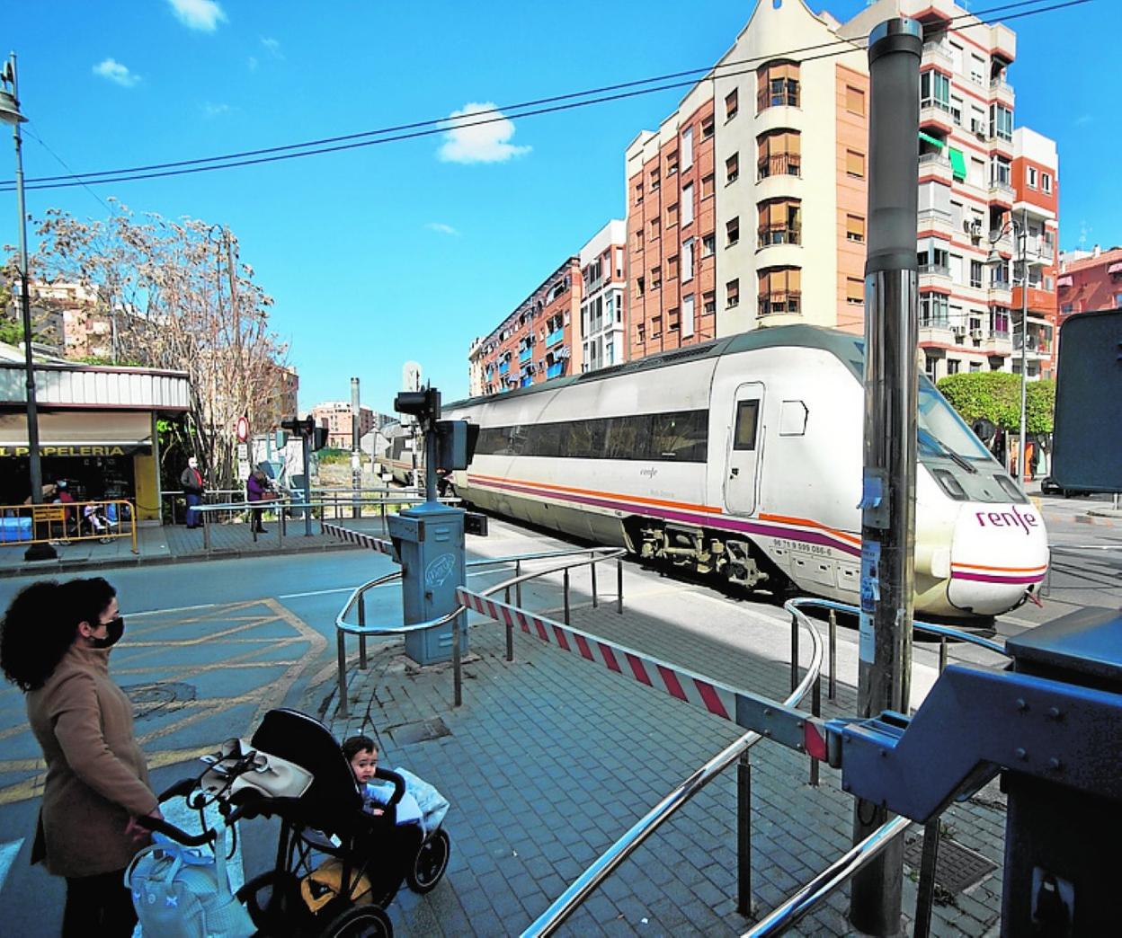 Una vecina con su hijo espera a que cruce el tren por la calle Mayor de Alcantarilla, el lunes. 