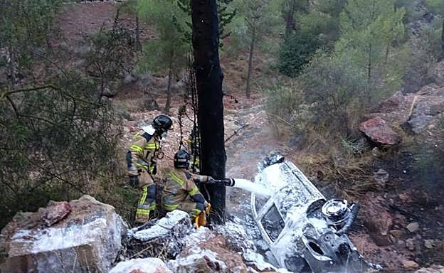 Bomberos sofocan las llamas en un coche que cayó por un barranco, en una fotografía de archivo. 