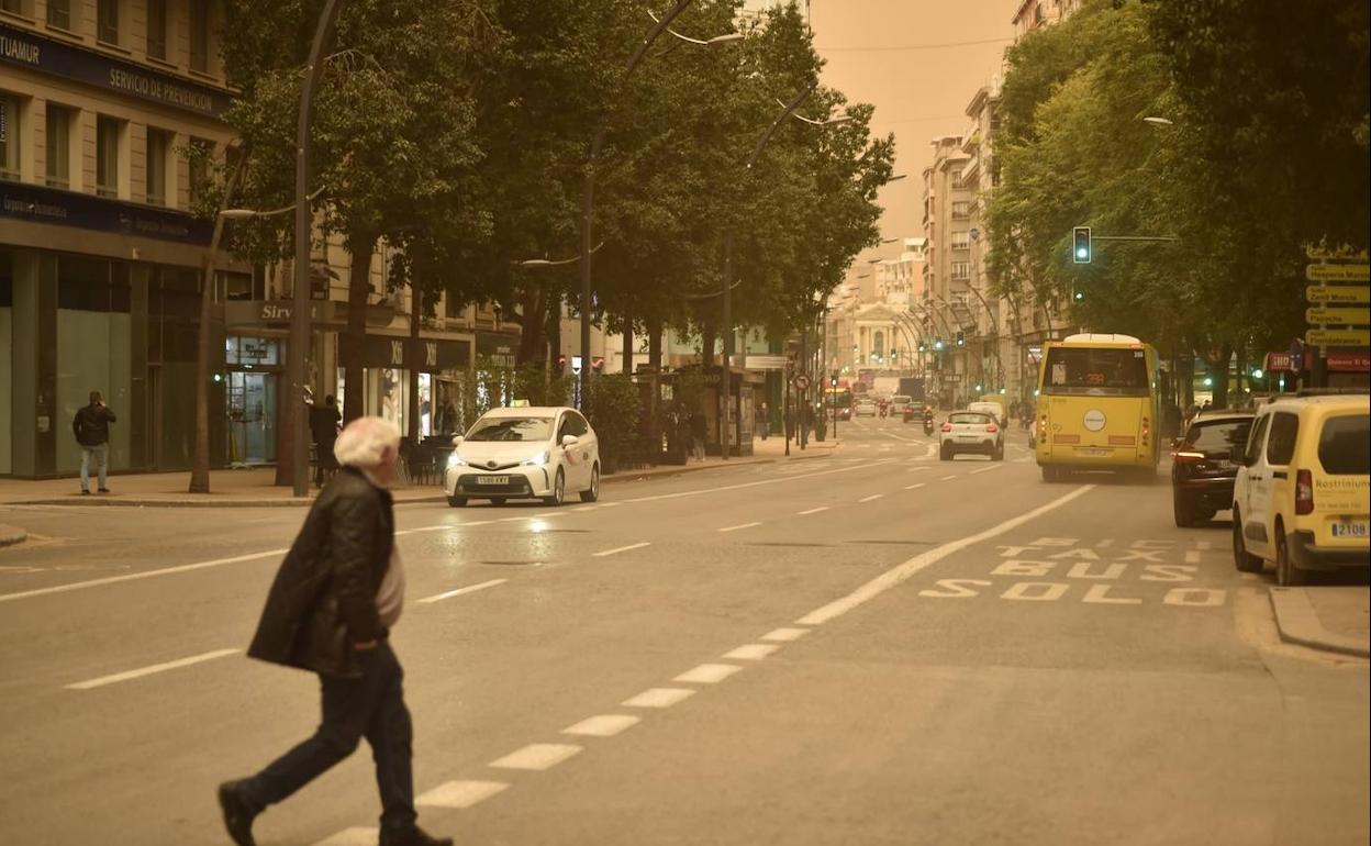 Un hombre cruza la Gran Vía de Murcia en el tercer día de calima en el cielo de la Región.