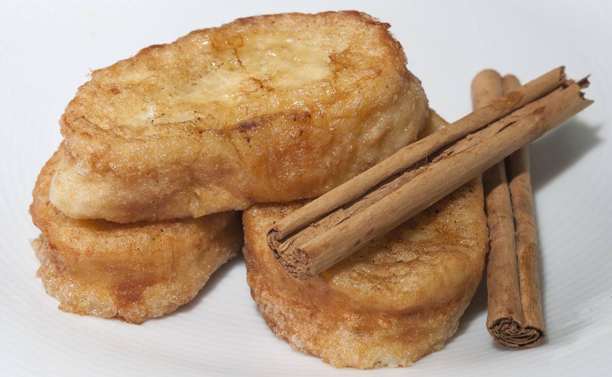 Unas torrijas servidas con dos ramas de canela.