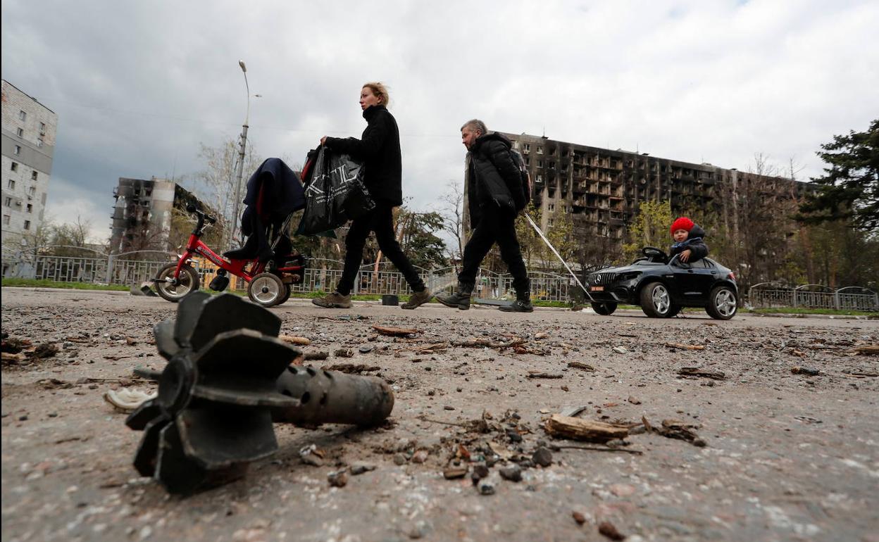 Miembros de una familia transitan por una calle de Mariúpol entre edificios bombardeados y restos de artillería. 