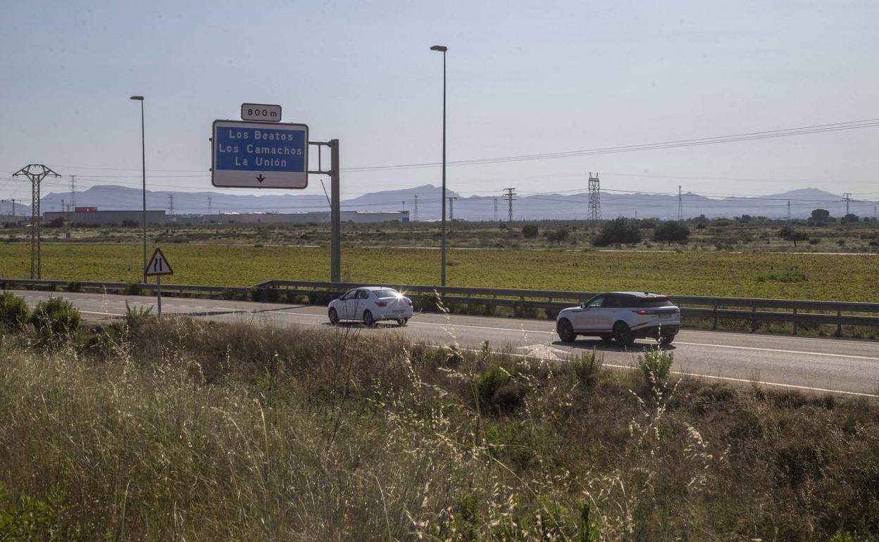 Dos coches pasan por una carretera que discurre paralela a los terrenos de la futura ZAL. 