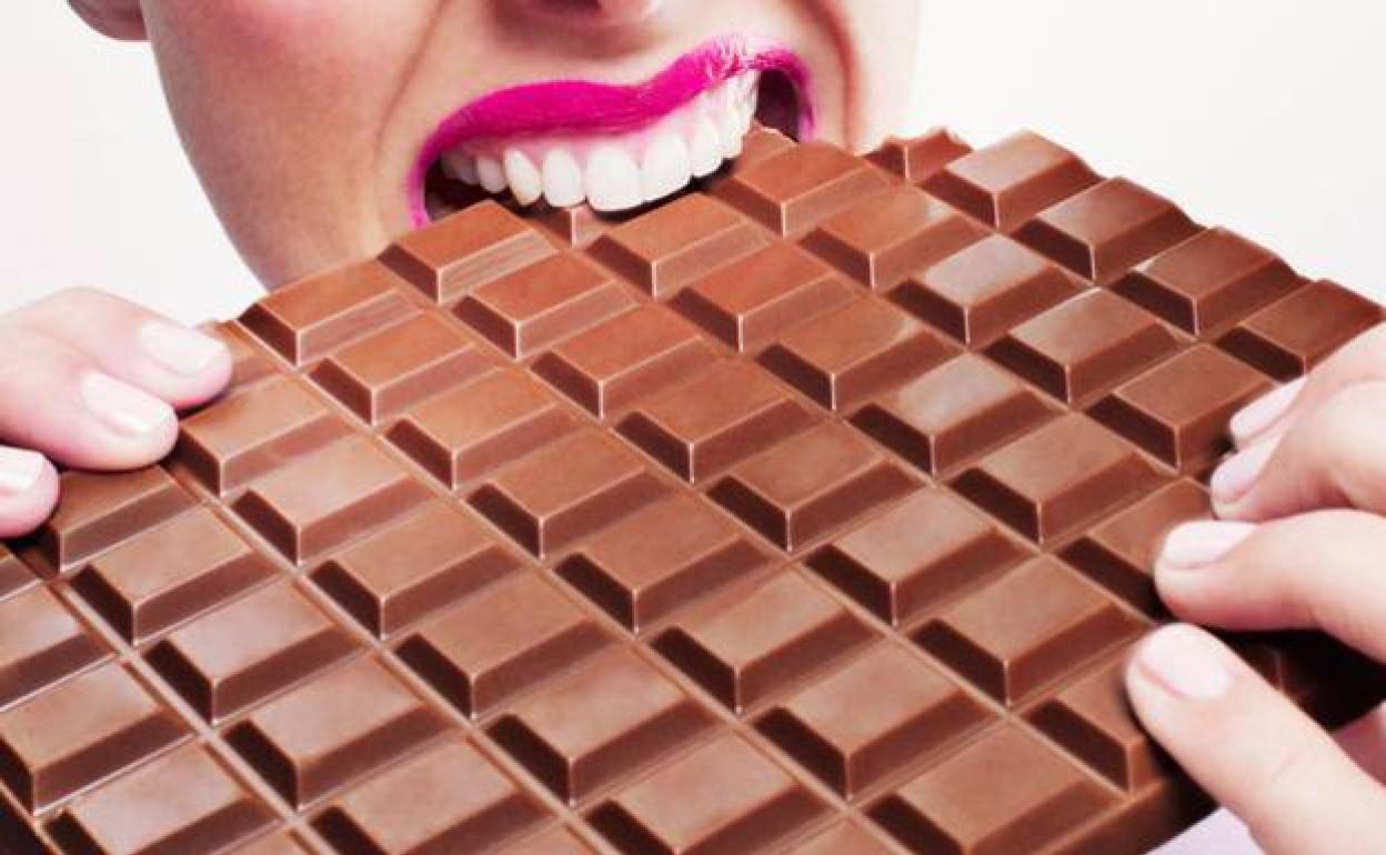 Una mujer muerde una tableta de chocolate.