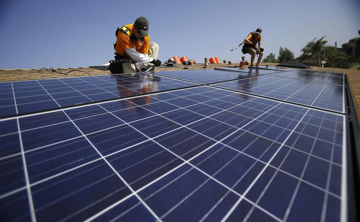 Dos operarios colocan paneles fotovoltaicos en la cubierta de un edificio. La fotografía es de archivo.