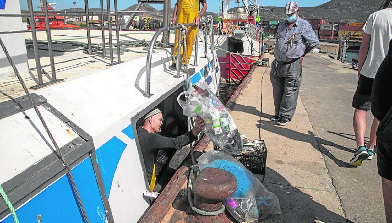 Un marinero saca una bolsa llena de plásticos retirados del mar. 
