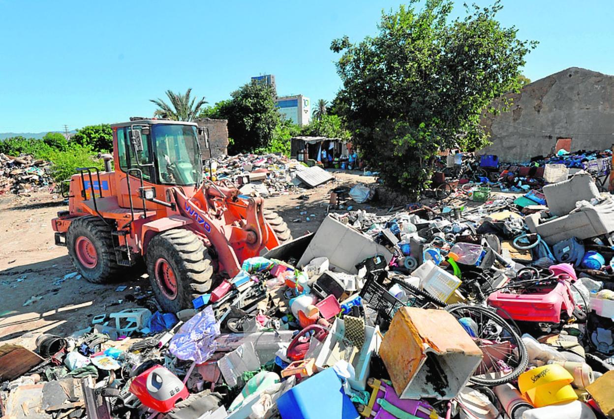 Una excavadora carga residuos acumulados en el asentamiento. 