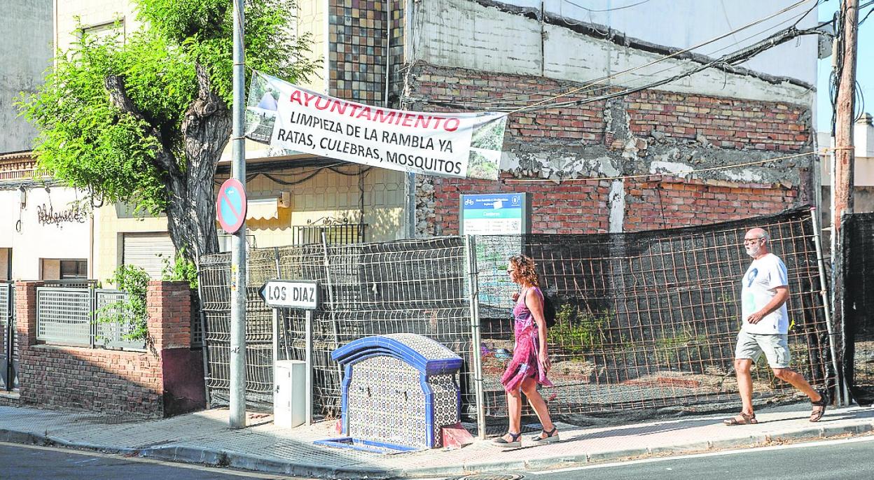 Dos vecinos pasan junto a la pancarta colocada entre la calle Mayor y la carretera de Los Díaz. 