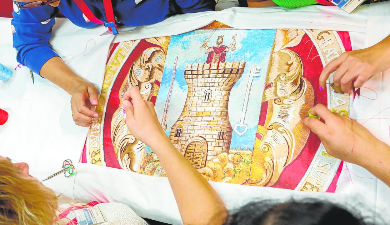 Las manos de cuatro bordadoras dan puntadas al escudo de la bandera de Lorca durante la celebración de Feramur. 