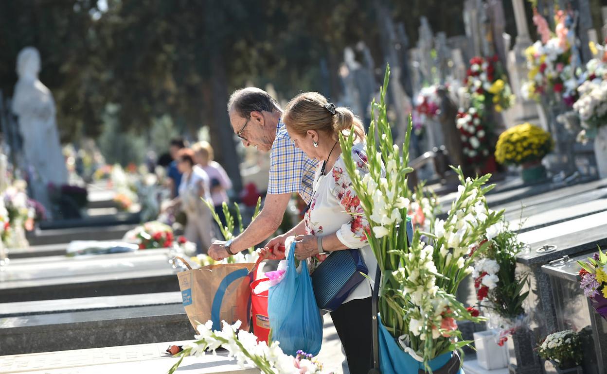 Una mujer y un hombre depositan flores en la tumba de un familiar, este martes, en Murcia.