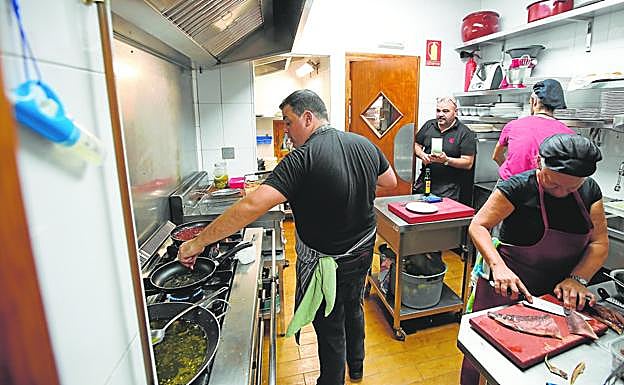 Juanfran atiende varios platos en los fogones mientras su madre corta bonito y su padre pasa unas comandas. 