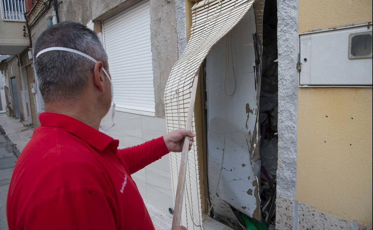Un operario descubre la puerta de la vivienda, desde la que se puede ver una pila de bolsas de basura. 