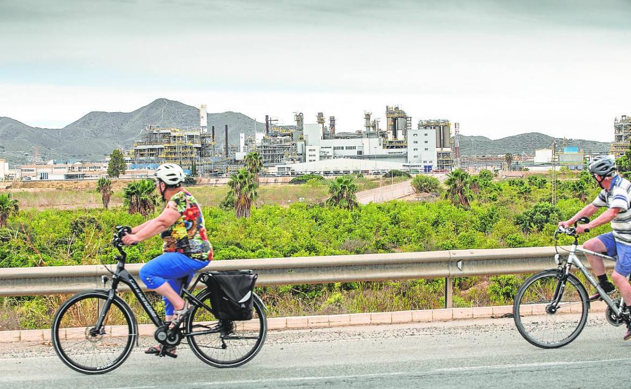 Dos ciclistas circulan por la carretera de Fuente Álamo, con la factoría de Sabic al fondo. 