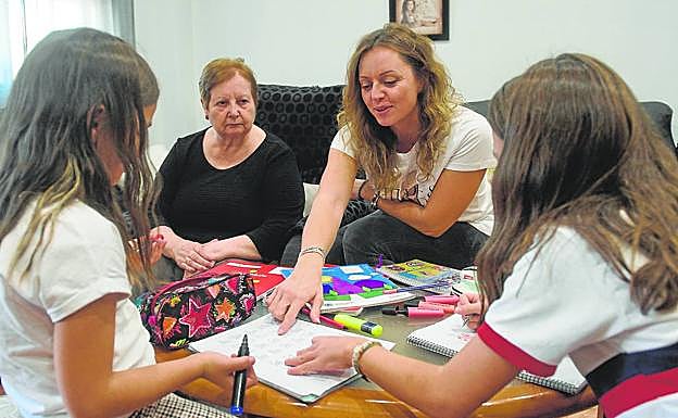 Fuensanta López, sentada junto a su madre, que padece alzhéimer, ayuda a sus hijas a hacer los deberes en su domicilio. 