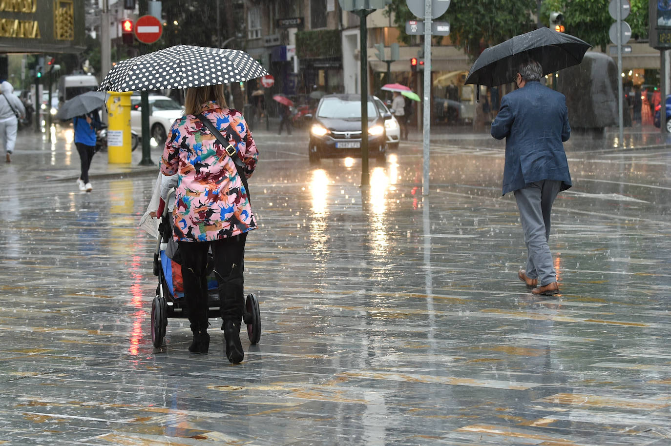 Dos personas caminan con paraguas bajo la lluvia en Murcia. 