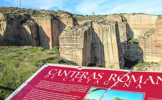 Canteras romanas al fondo, con un cartel informativo en primer plano que divulga el valor de este yacimiento arqueológico. 