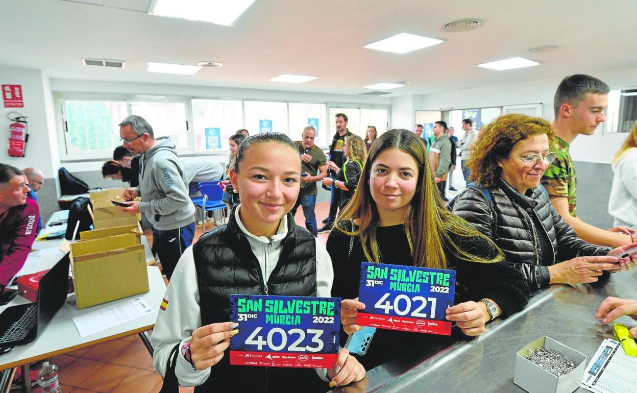 Dos participantes en la carrera de fin de año de Murcia muestran su dorsal, en el Príncipe de Asturias. 