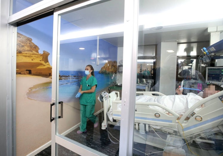 Una sanitaria atiende a un paciente en un 'box' de la UCI del Morales Meseguer, decorado con la imagen de la playa de Los Cocedores, en Águilas.