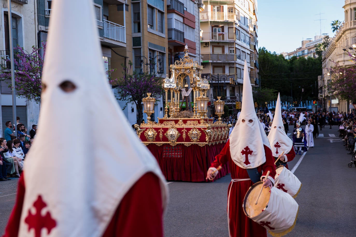 El trono, que representa un calvario y sobre el que se incriben los escudos de todas las cofradías de la Semana Santa oriolana, es obra de los hermanos orfebres Martínez Vicente y data de 1978.