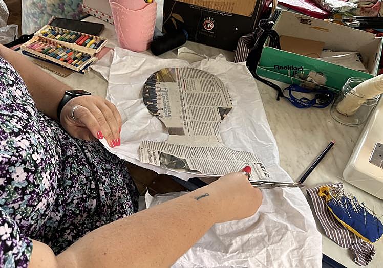 Inés Serrano coloca sobre una tela doble el molde de una cabeza con papel de periódico para recortar la tela, que posteriormente se cose a maquina para tener lo que será la cabeza del mayo.