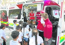 Tres voluntarios enseñan una ambulancia de Cruz Roja a un grupo de escolares, en Juan XXIII.