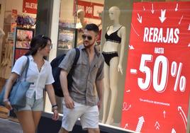 Dos jóvenes pasan delante de un escaparate con un cartel de rebajas, en una imagen de archivo.