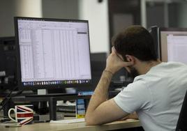 Un trabajador mira con actitud cansada una pantalla de ordenador en una oficina.