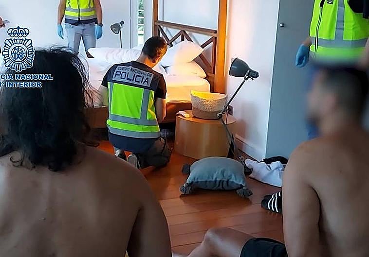 Dos detenidos observan cómo los agentes inspeccionan un dormitorio de la vivienda en la que se encontraban.