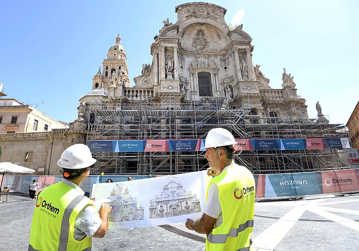 Dos trabajadores sujetan el plano de la Catedral de Murcia frente al andamio.