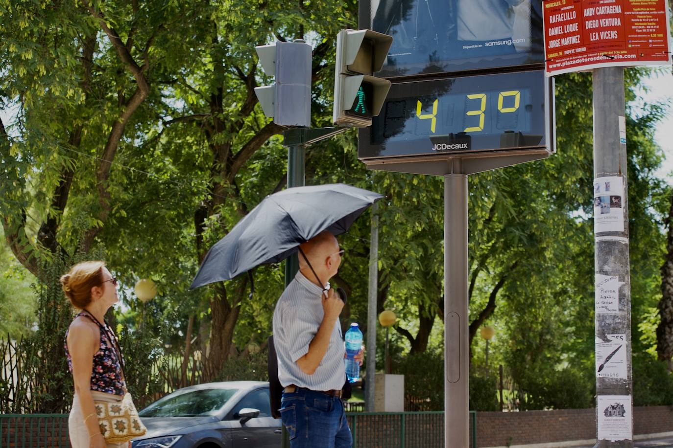 Un hombre se protege del sol con un paraguas junto a uno de los termómetros del centro de Murcia.