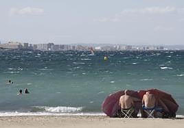 Dos hombres se protegen del viento, este domingo en una playa de Cabo de Palos.