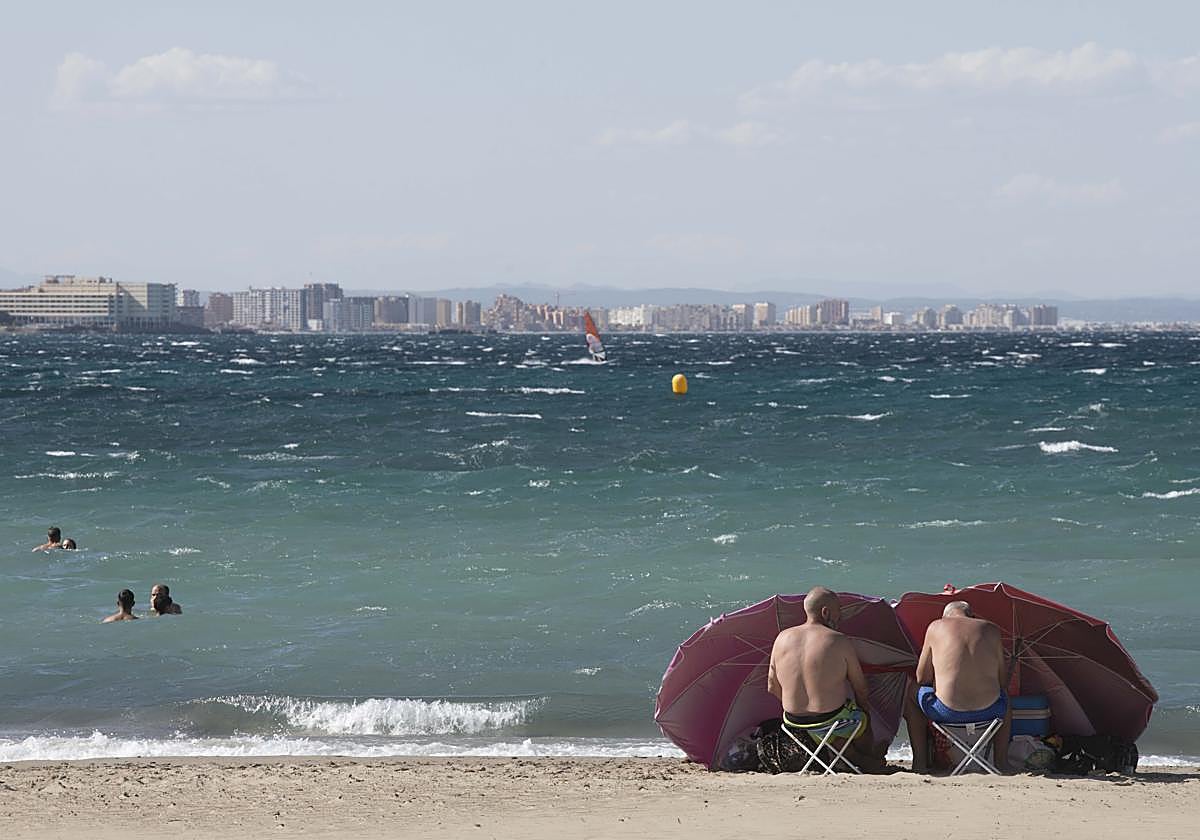 Dos hombres se protegen del viento, este domingo en una playa de Cabo de Palos.