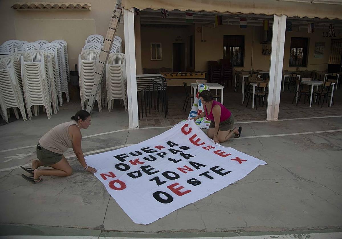 Dos vecinas de Los Puertos de Santa Bárbara preparan una pancarta contra la explotación de Cemex, hace unos días.