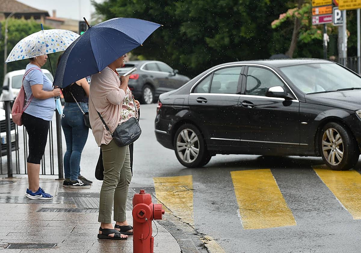 Unas mujeres con su paraguas esperan para cruzar la calle.