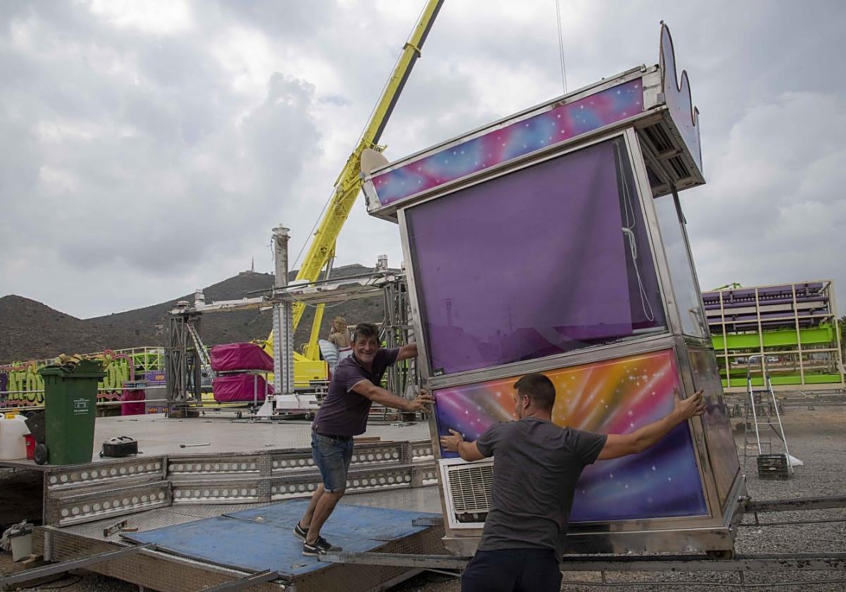 Dos feriantes colocan la taquilla de una de las atracciones infantiles en el parking del centro comercial Rambla.