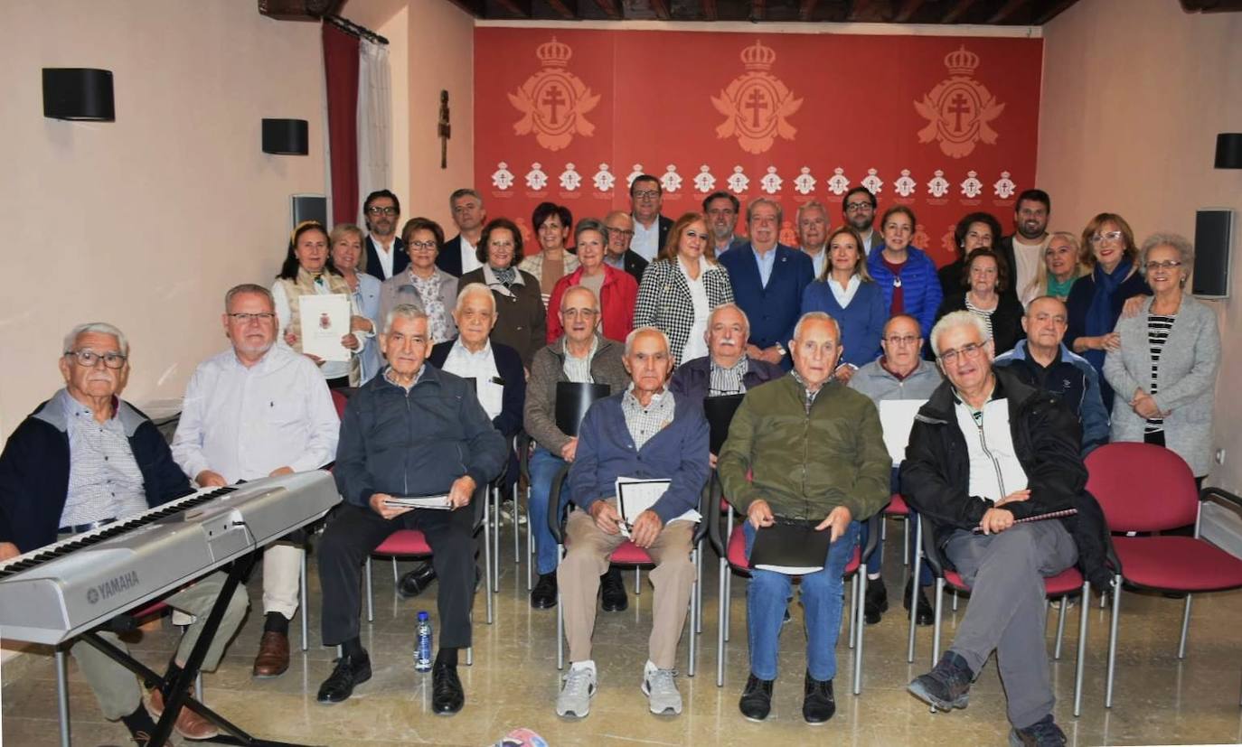 Parte de los componentes del coro de El Salvador posan junto a parte de la Junta Representativa de la Cofradía de la Vera Cruz en el Salón de Actos de la Casa de la Cruz.