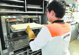 Una empleada de la estación de servicios de Repsol de la ICA (Murcia) introduce en un horno una bandeja con barras de pan.