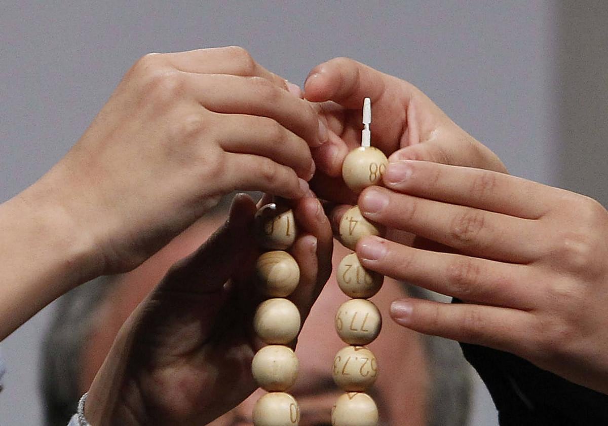 Primer plano de las manos de dos niños de San Ildefonso mientras encajan dos bolas de la Lotería de Navidad en los alambres