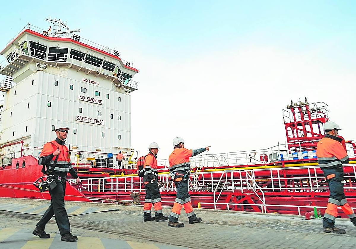 Cuatro operadores se disponen a descargar aceites usados del 'Med Arctic' en el muelle de Repsol.