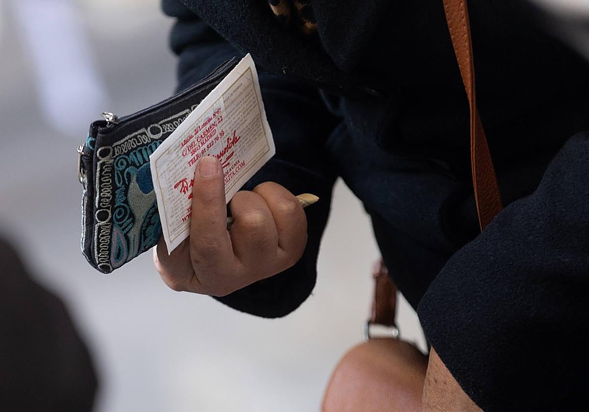 Una persona sujeta con su mano un monedero azul y un décimo de la Lotería de Navidad 2023