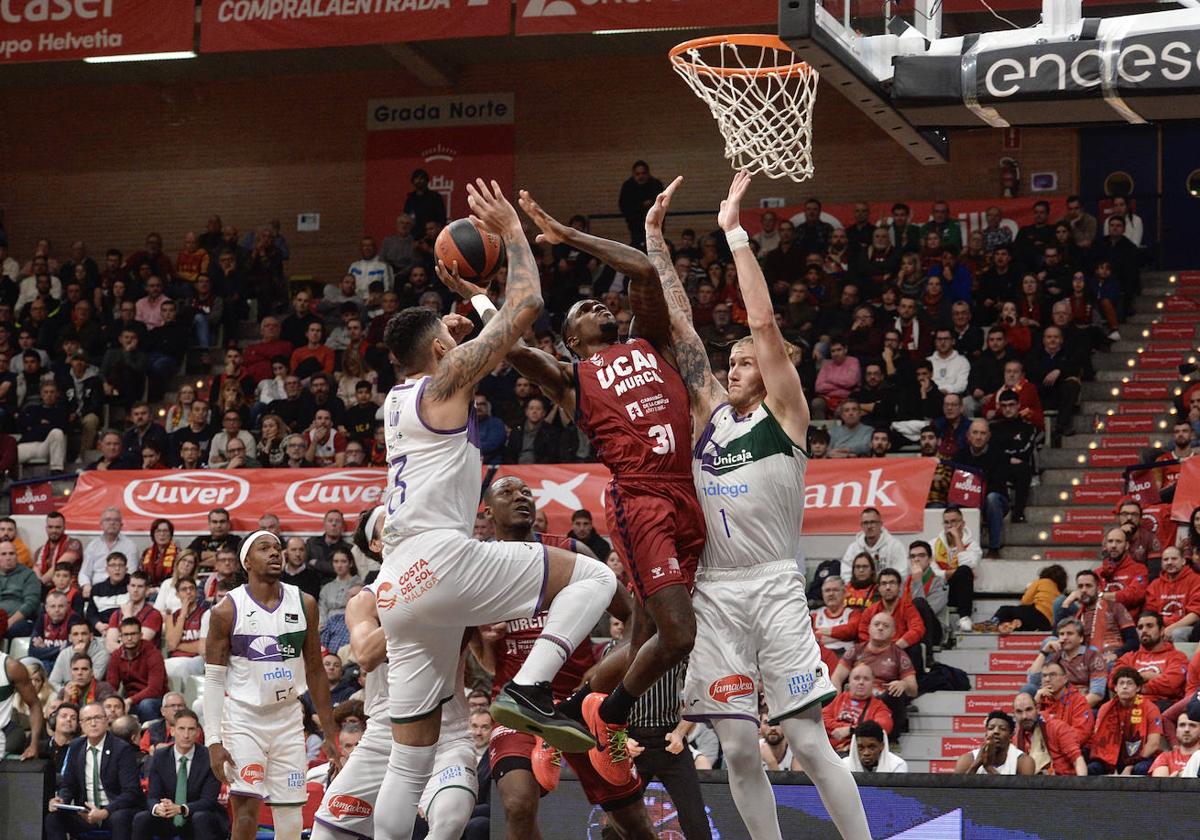 El jugador del UCAM Dylan Ennis entra a canasta, acosado por el exuniversitario Augusto Lima y Osetkowski, anoche.