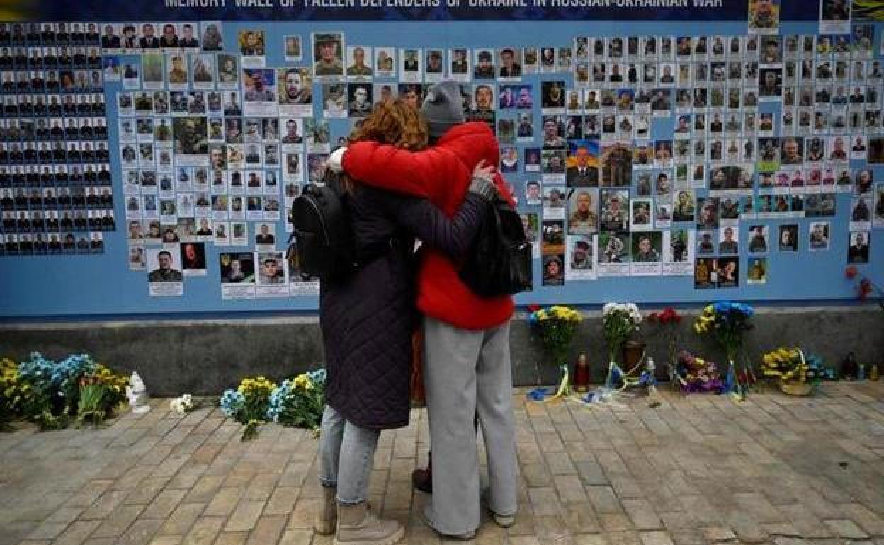 Dos mujeres observan el muro con los retratos de los fallecidos en la guerra de Ucrania