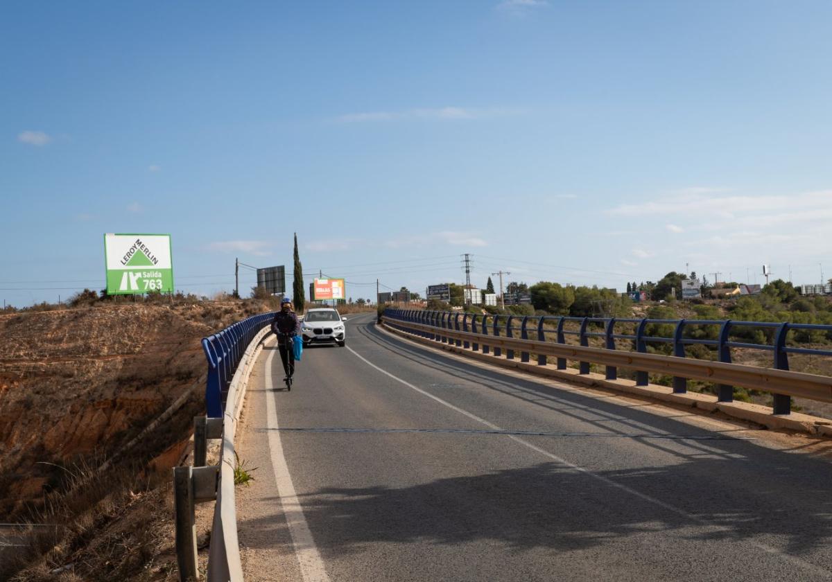 Un patinete transita por la calzada del puente sobre la AP-7, que carece de carril bici o acera.