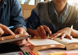 Tres estudiantes realizan una tarea frente al ordenador y bajo la supervisión de un docente.