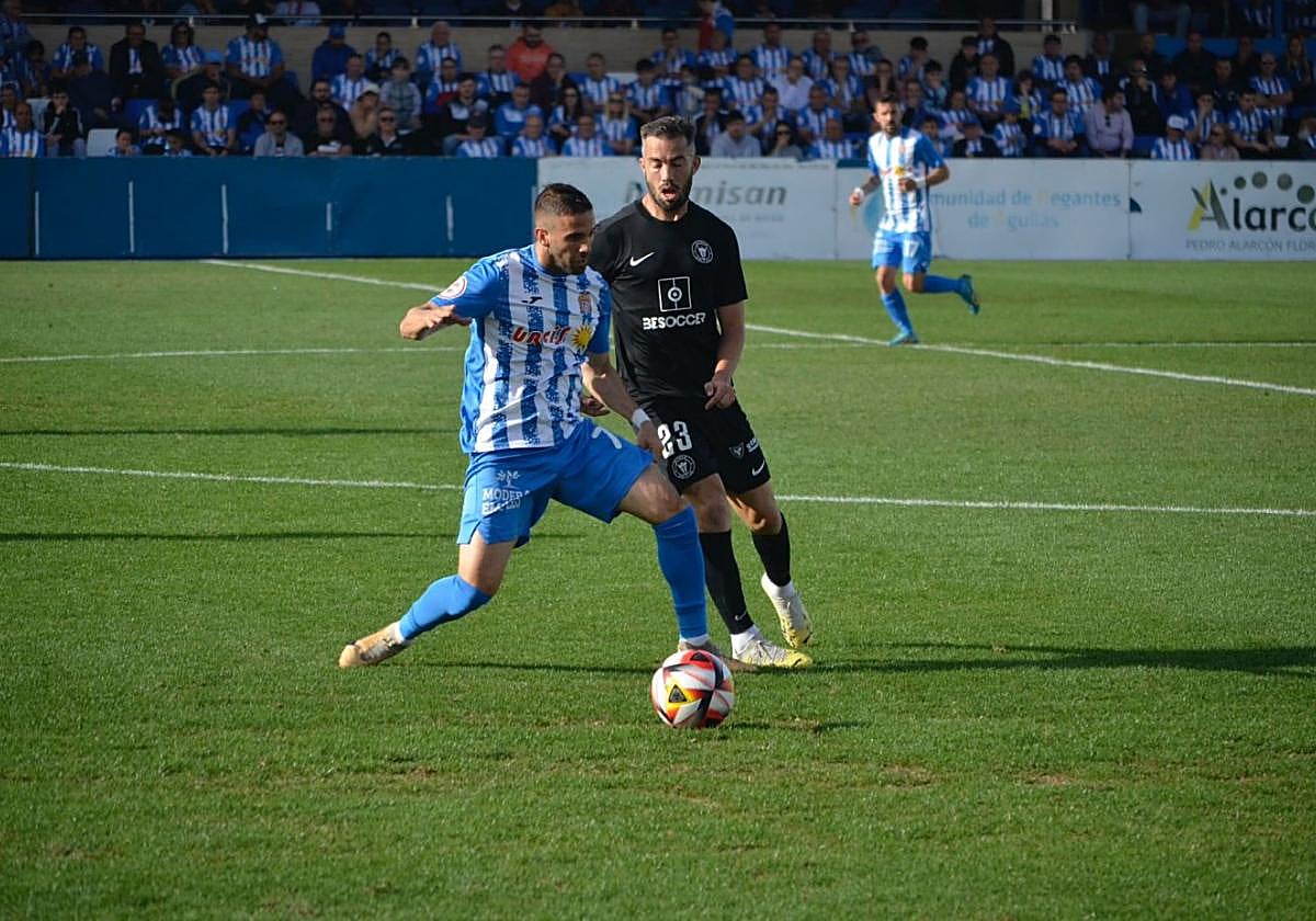 Víctor Fenoll, del Águilas, protege el balón ante la presión del visitante Santi Luque.