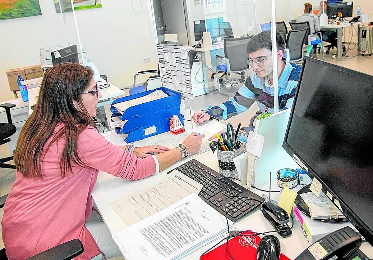 Una funcionaria atiende a un vecino en Torre Pacheco de forma manual, mientras el ordenador de su mesa permanece apagado.